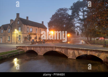 Dunst und Nebel kurz nach Sonnenaufgang in der cotswold Dorf Bourton auf dem Wasser im Herbst. Bourton auf dem Wasser, Cotswolds, Gloucestershire, England Stockfoto