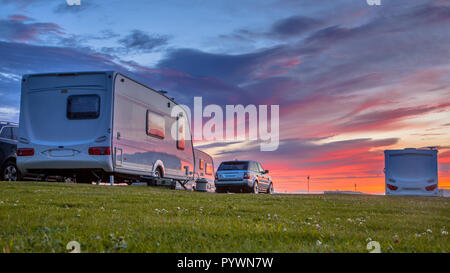 Wohnwagen und Autos auf einem grasbewachsenen Campingplatz im Sommer geparkt unter schönen Sonnenuntergang Stockfoto