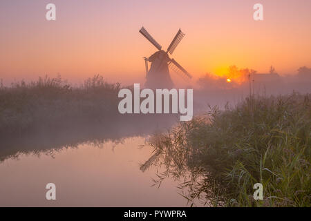 Charakteristische historische Windmühle entlang eines Flusses in einem Polder Feuchtgebiet an einem nebligen Septembermorgen in den Niederlanden Stockfoto