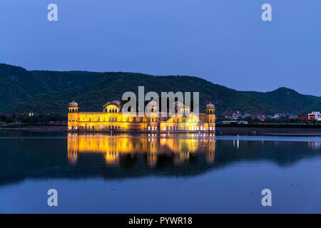 Beleuchtete Jal Mahal Palast bei Nacht in Jaipur, Indien. Beliebte Sehenswürdigkeit von Wasser umgeben. Berge im Hintergrund Stockfoto