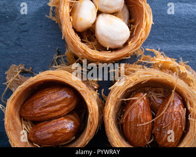 Nahaufnahme Makro von drei türkische Baklava mit Mandeln und Haselnüsse. Von oben flach auf schwarzem Schiefer Hintergrund Schuß Stockfoto