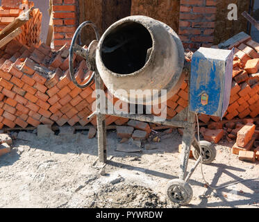 Nahaufnahme der Betonmischer bei schmutzigen Baustelle in der Nähe von Packs Paletten aus roten Ziegeln. Sommer 12.00 Uhr, Außenansicht Stockfoto