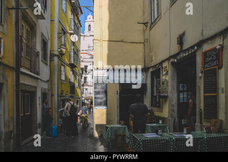 Lissabon, Portugal - 24.Oktober 2018: Straßen mit traditionellen Restaurants im Stadtteil Alfama von Lissabon mit Sao Vicente Kirche im Hintergrund Schmal Stockfoto