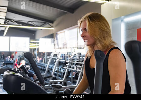 Junge passende Frau an der Turnhalle mit elliptischen Crosstrainer. Sportlerin im Fitnessraum trainieren auf dem Hometrainer Stockfoto