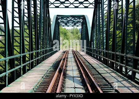 Grün metall Eisenbahnbrücke Konstruktion mit Eisenbahnschienen mit mehreren verrostete Schrauben und Muttern verbunden und mit hölzernen Gehweg umgeben Stockfoto