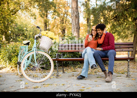 Multiratial Paar sitzt auf der Bank im Herbst City Park Stockfoto