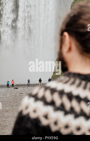 Eine isländische Reiseführer Tragen eines traditionellen Lopapeysa Isländische wolle Pullover am Wasserfall Skogafoss im Süden Islands. Schwerpunkt der Version Stockfoto