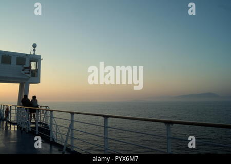 Sonnenuntergang vom Deck einer Inter Insel Fähre, wie es über die Ägäis in Griechenland segelt. Zwei Passagiere beobachten den Sonnenuntergang. Speicherplatz kopieren. Stockfoto