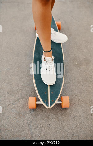 Nahaufnahme von Frau Beine in weißen Turnschuhen auf Longboard Stockfoto