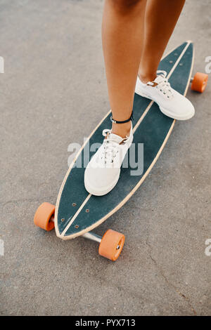 Nahaufnahme von Frau Beine in weißen Turnschuhen auf Longboard Stockfoto