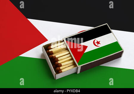 Westsahara Flagge ist in einer offenen Streichholzschachtel, die mit Streichhölzern gefüllt ist und liegt auf einer großen Flagge gezeigt. Stockfoto