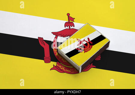 Brunei Darussalam Flagge ist abgebildet auf eine Streichholzschachtel, die auf eine grosse Fahne liegt. Stockfoto