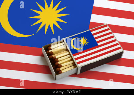 Malaysia Fahne ist in einer offenen Streichholzschachtel, die mit Streichhölzern gefüllt ist und liegt auf einer großen Flagge gezeigt. Stockfoto