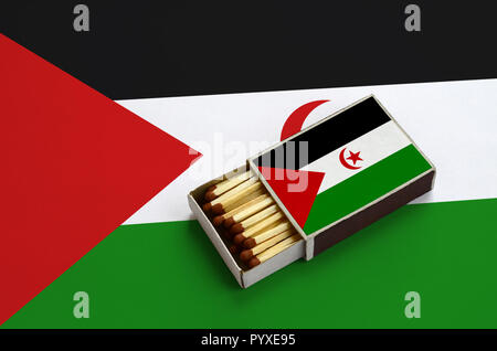 Westsahara Flagge ist in einer offenen Streichholzschachtel, die mit Streichhölzern gefüllt ist und liegt auf einer großen Flagge gezeigt. Stockfoto