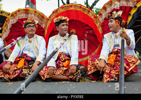Bali, Indonesien - 23. Juni 2018: Die Gruppe der jungen Tänzerin Männer in ethnischen Kostüme mit traditionellen Rot Schwarz und Gelb Schirme am hinduistischen Zeremonie Parade Stockfoto
