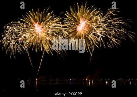 Goldene riesen Feuerwerk Raketen Explosionen in Nacht über Wasser Stockfoto