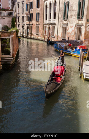 Eine Gondelbahn führt durch einen Patch von Sun auf dem Wasser von einem Kanal in Venedig, Italien Stockfoto