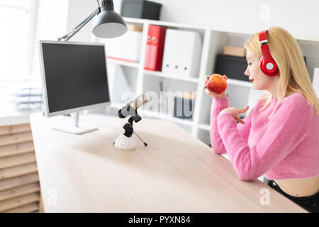 Ein junges Mädchen mit Kopfhörern am Tisch sitzen und mit einem Apfel. Stand vor ihr Mikrofon. Stockfoto