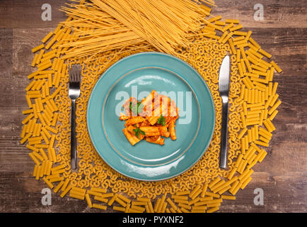 Teller Pasta a la arribiata mit verschiedenen Arten von Nudeln in kreisförmigen Schichten mit leeren Raum in der Platte Gabel und Messer Bereiche in einem alten Vintage Woo Stockfoto