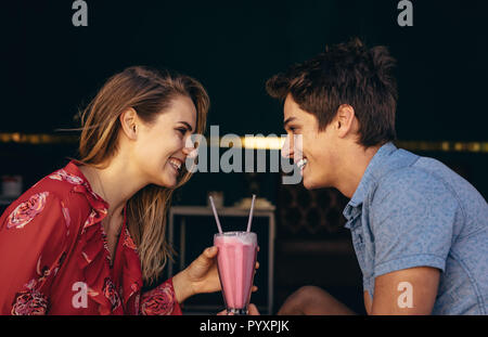Romantisches Paar auf einem Datum Sitzen im Freien in einem Milchshake mit zwei strohhalme. Paar an jedem anderen sitzen in einem Restaurant suchen. Stockfoto