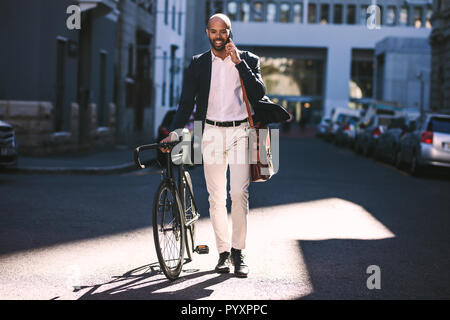 Portrait der afrikanischen Mann zu Fuß mit dem Fahrrad zur Arbeit und am Telefon sprechen. Business Mann, Büro mit seinem Fahrrad. Stockfoto