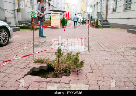 Lodz, Polen, Juli 2018. Ein Loch im Bürgersteig mit einem wachsenden Bush innen, umzäunten das rote und das weiße Band. Stockfoto