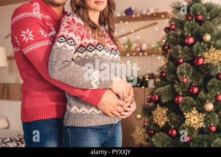Zugeschnittenes Bild von Mann umarmt die schwangere Frau in der Nähe von Weihnachten zu Hause Stockfoto