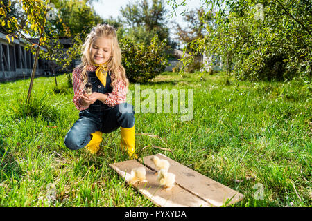 Glückliches Kind sitzen auf Gras in der Nähe von Yellow Baby Küken auf der Farm Stockfoto