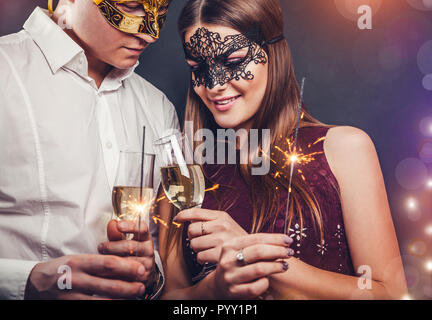 Paar feiert New Year's Eve trinken Champagner und Beleuchtung bis Wunderkerzen auf der Maskerade Partei Stockfoto