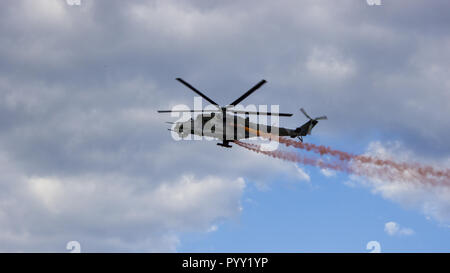 Kampfhubschrauber mit roten Rauch auf blauer Himmel mit weißen Wolken. Ansicht von unten. Stockfoto