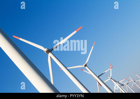 Horizontale gewinkelte Blick auf viele weiße äolischen Windenergieanlagen in einem Energie Farm gegen einen klaren blauen Himmel mit Copyspace Stockfoto