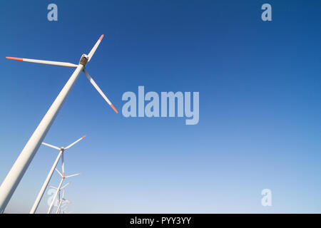 Horizontale gewinkelte Blick auf Zeile weiß äolischen Windenergieanlagen in einem Energie Farm gegen einen klaren blauen Himmel mit Copyspace Stockfoto