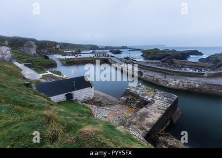 Mit Blick auf einen kleinen Hafen mit Felsvorsprüngen auf einem nebligen Morgen umgeben. Drehort der TV-Serien HBO Spiel der Throne. Ballintoy, County Antrim Stockfoto