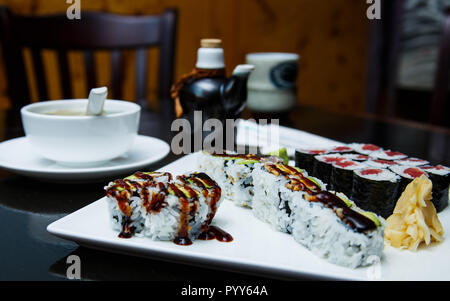 Frisches Sushi rollen, Misosuppe und ein Glas Soja Sauce auf einen dunklen Tisch. Stockfoto