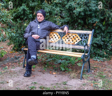 Älterer Mann sitzt auf dekorativen schmiedeeisernen & Holz Werkbank, Besinnlich, nachdenklich, traurig. Stockfoto