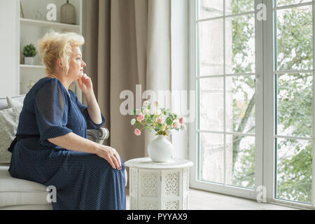 Ältere Frau sitzt auf dem Sofa und schauen sich die Fenster zu Hause Stockfoto