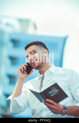 Fröhlicher Kerl über sein Smartphone im Freien während Buch Stockfoto