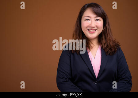 Reifen schöne asiatische Geschäftsfrau gegen braunen Hintergrund Stockfoto