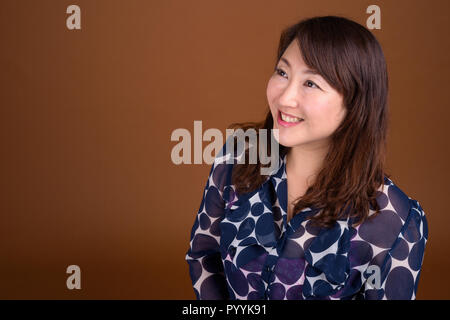Reifen schöne asiatische Geschäftsfrau gegen braunen Hintergrund Stockfoto