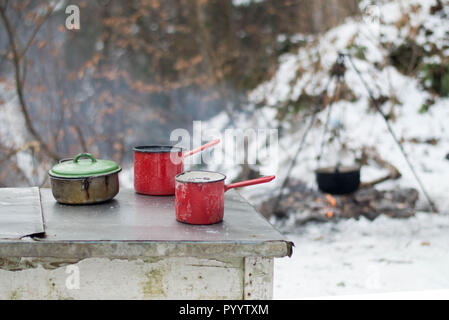 Emaille Geschirr auf dem Tisch - Kochen im Freien im Winter mit Lagerfeuer im Wald Stockfoto