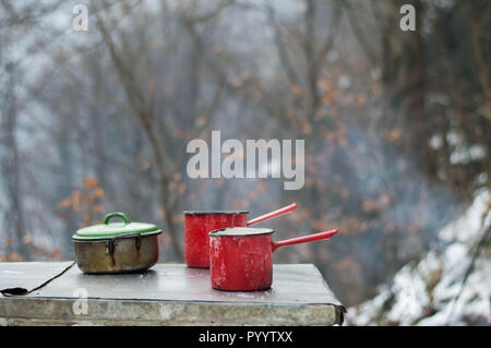 Emaille Geschirr auf dem Tisch - Kochen im Freien im Winter mit Lagerfeuer im Wald Stockfoto