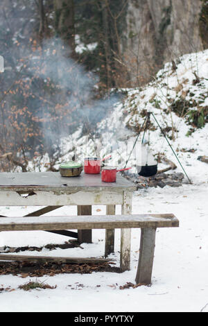 Emaille Geschirr auf dem Tisch - Kochen im Freien im Winter mit Lagerfeuer im Wald Stockfoto