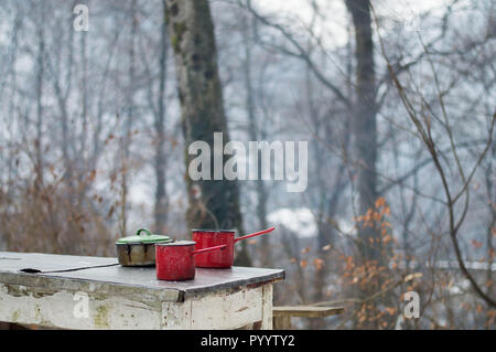 Emaille Geschirr auf dem Tisch - Kochen im Freien im Winter mit Lagerfeuer im Wald Stockfoto