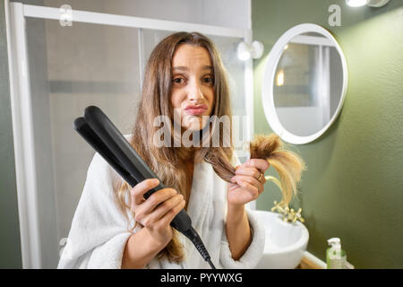 Portrait von unglücklichen Frau mit Splitting Haarspitzen und Haarglätter im Badezimmer Stockfoto