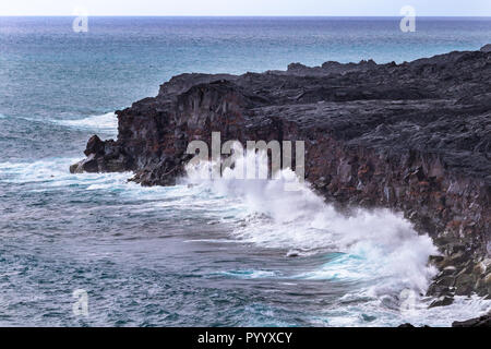 Große Wellen gegen hohen vulkanischen Felsen auf Hawaii Big Island, im Volcano National Park. Pazifik im Hintergrund. Stockfoto