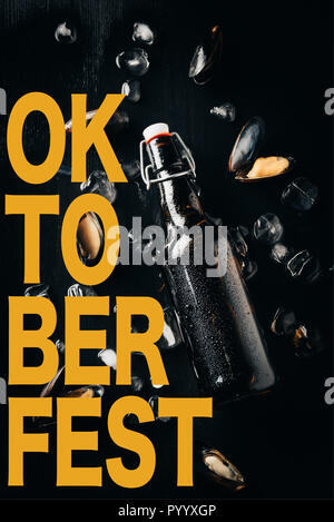 Flach mit einer Flasche Bier, Muscheln und Eiswürfel auf dunklen Tischplatte mit 'Oktoberfest' Schriftzug angeordnet Stockfoto