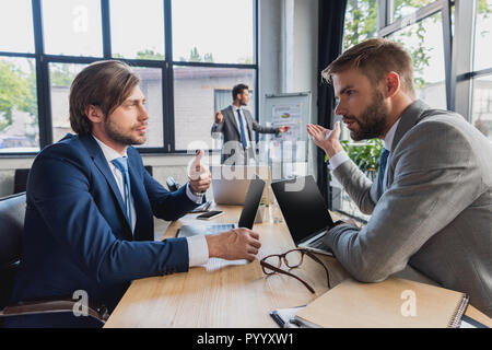 Seitenansicht der jungen Geschäftsleute mit Laptops und diskutieren Projekt im Büro Stockfoto