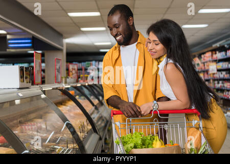 Lächelnd afrikanische amerikanische Paar mit Einkaufswagen wählen Sie Lebensmittel im Supermarkt Stockfoto