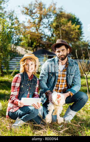 Erzeuger, Huhn, während seine Freundin mit digitalen Tablet in der Nähe an der Ranch Stockfoto