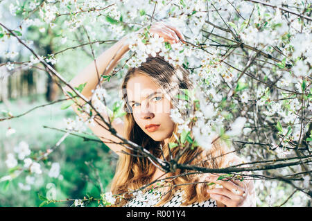 Porträt eines jungen Mädchens in der Blüte Cherry Garden, das Berühren eines Zweige, mit Blick auf die Kamera Stockfoto